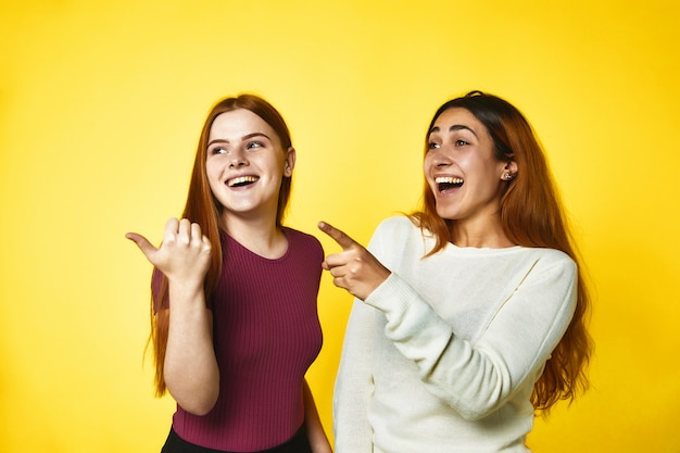 Two young girls are pointing fingers aside and laughing standing 