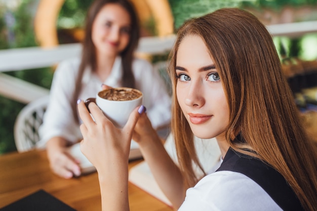 Two young girls looking to the camera in the cafe with coffe