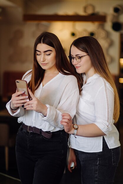 Две молодые девушки с помощью смартфона в кафе