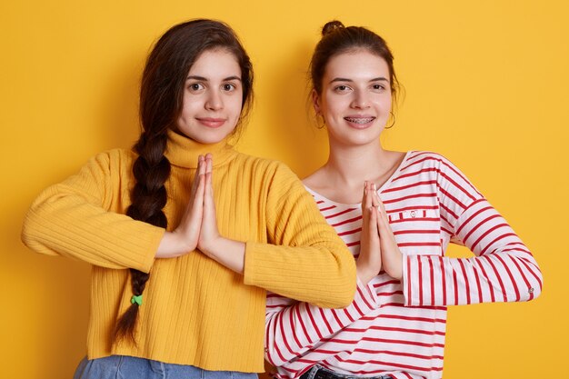 Two young girls wearing casual shirts posing with palms together and smiling