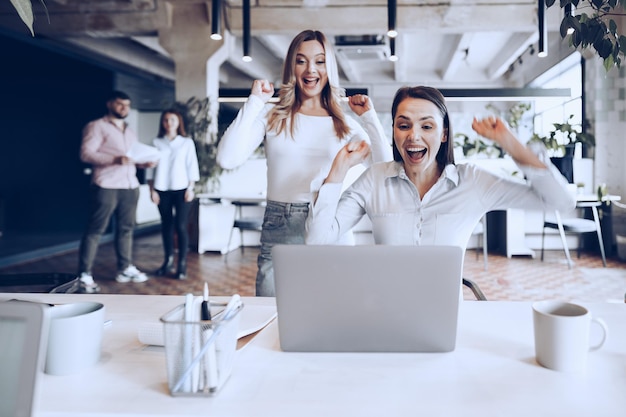 Две молодые счастливые бизнес-леди празднуют успех проекта в офисе