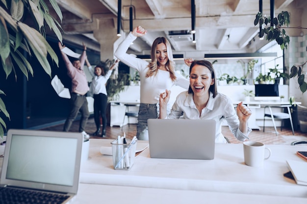 Two young happy businesswomen celebrating project success in office