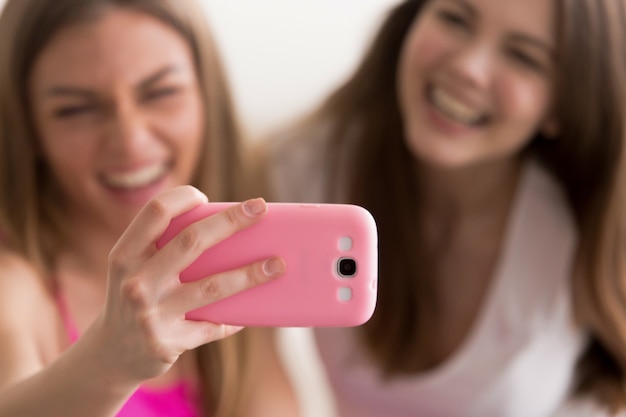 Two young happy girlfriends taking selfie with smart phone.