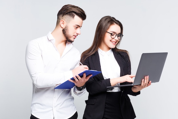 Two young happy smiling successful businesspeople working with laptop on white wall