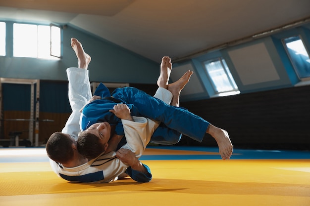 体育館で武道を訓練する着物姿の2人の若い柔道選手が、動きと動きを表現しています。