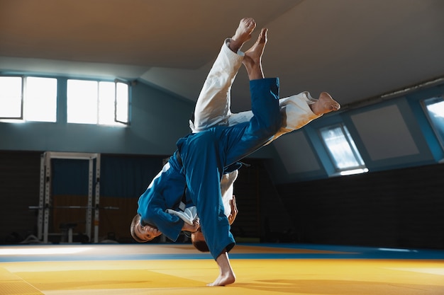 Two young judo fighters in kimono training martial arts in the gym with expression in action and motion