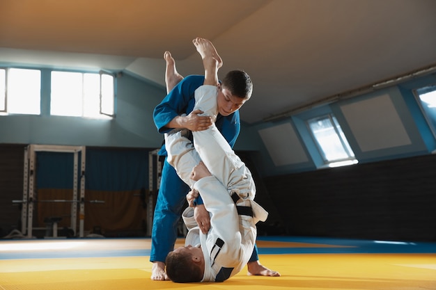 Двое юных дзюдоистов в кимоно тренируют боевые искусства в тренажерном зале