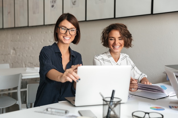 Two young laughing women working by the table