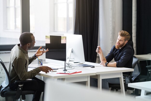 Two young male colleagues sitting at opposing desks