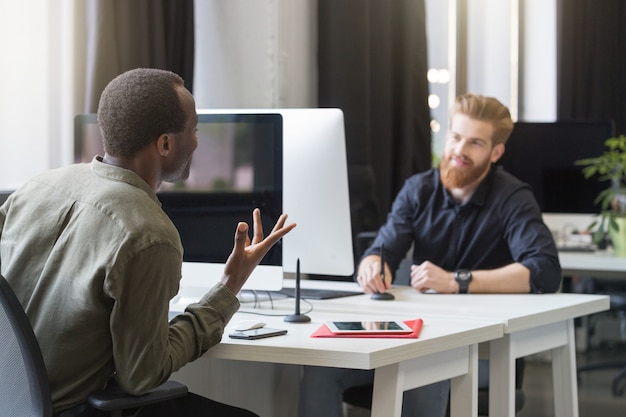 Two young male colleagues sitting at opposing desks