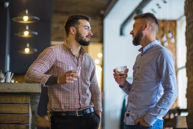 Two young male friends holding glass of drinks standing at bar counter