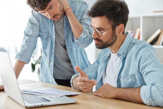 Two young man entrepreneurs work together on financial report, look attentively at documents