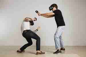 Бесплатное фото Два молодых человека в шлемах виртуальной реальности дерутся, мужчина в черной футболке бьет, а мужчина в белой футболке прячется и прячется.
