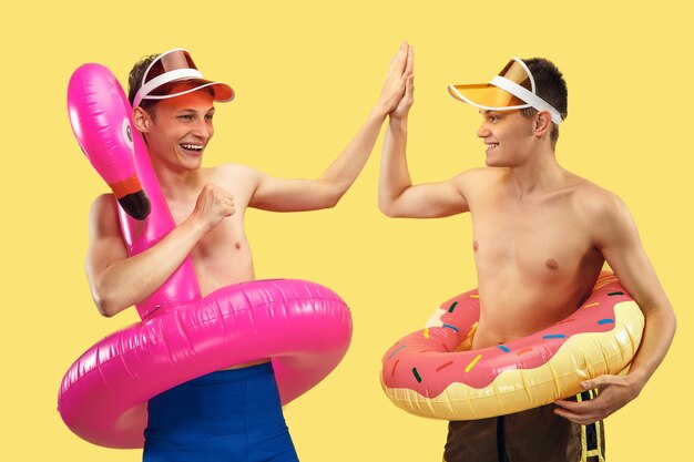 Two young men's half-length portrait isolated. Smiling friends in caps with swimrings. Facial expression, summer, weekend, resort or vacation concept. Trendy colors.