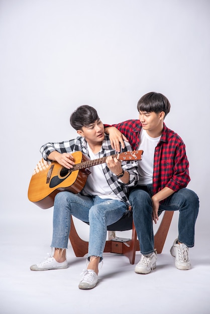 Two young men sat on a chair and played guitar.