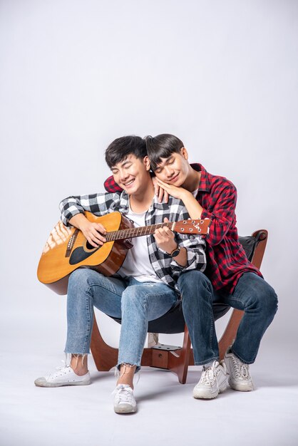 Двое молодых людей сидели на стуле и играли на гитаре.
