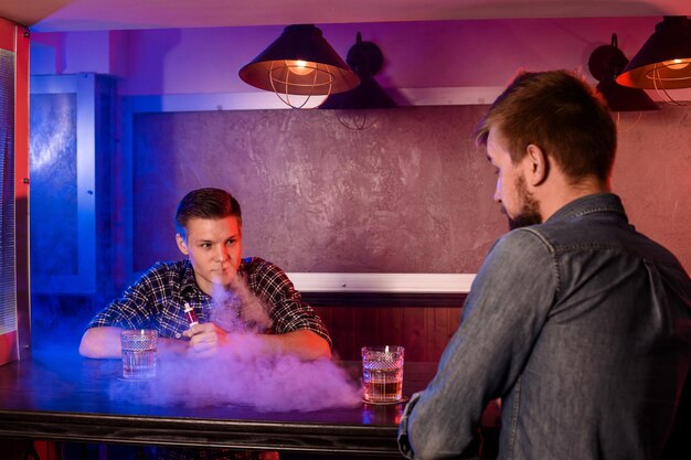2人の若い男性がvapebarで電子タバコを吸います。アークショップ