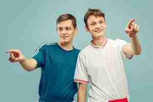 Free photo two young men standing in sportwear isolated. fans of sport, football or soccer club or team. friends' half-length portrait. concept of human emotions, facial expression.