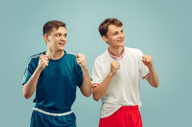 Two young men standing in sportwear isolated. Sport's team fans. Beautiful male models' half-length portrait. Concept of human emotions, facial expression. Front view.