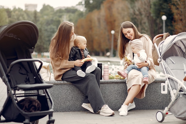 Two young mothers sitting in a autumn park with carriages