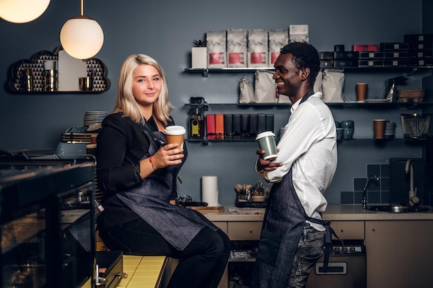 Two young multiracial baristas relaxing after work day in a coffee shop or cafe