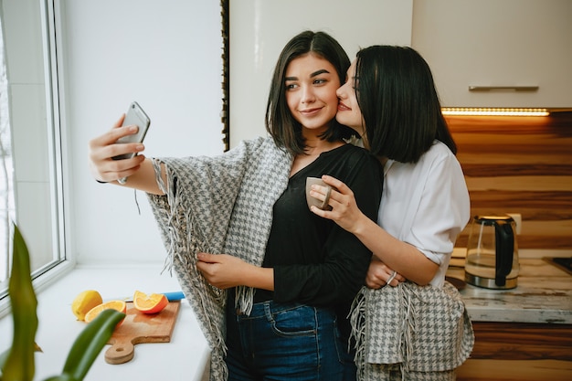 two young and pretty brunette standing by the window in the kitchen with orange