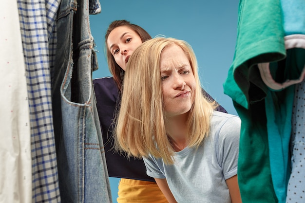 Foto gratuita le due giovani belle ragazze che guardano i vestiti e provano mentre scelgono in negozio