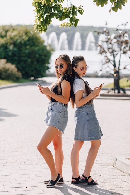 Две молодые красивые девушки на прогулке в парке с телефонами. солнечный летний день, радость и дружба.