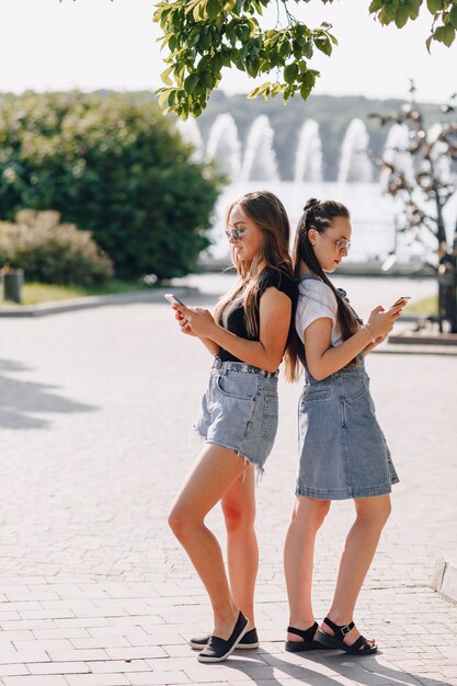 Two young pretty girls on a walk in the park with phones