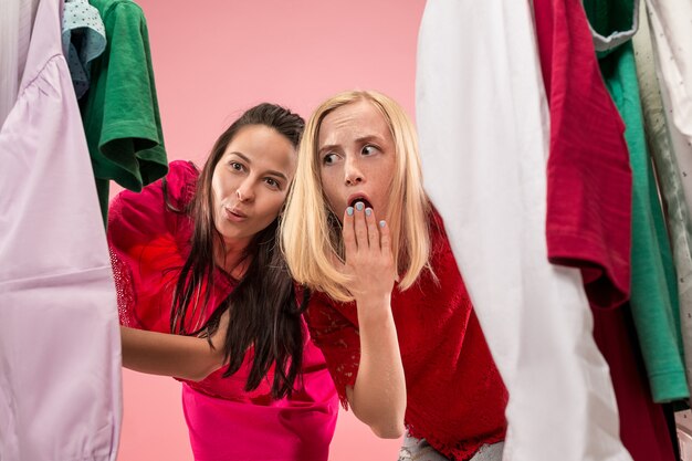 Две молодые красивые женщины смотрят на платья и примеряют их, выбирая в магазине