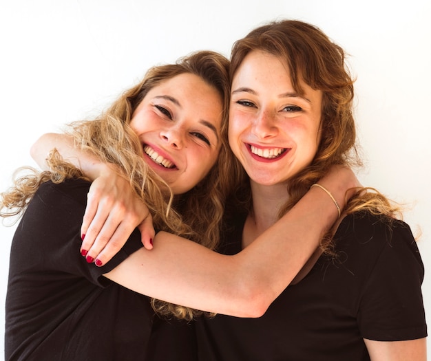 Две молодые сестры, обнимая друг друга на белом фоне