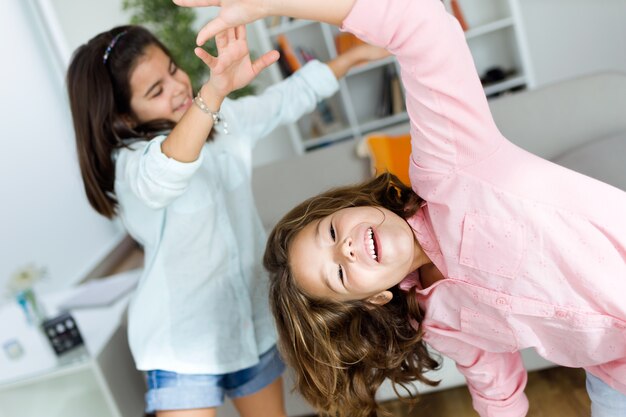 Two young sisters listening to music and dancing at home.