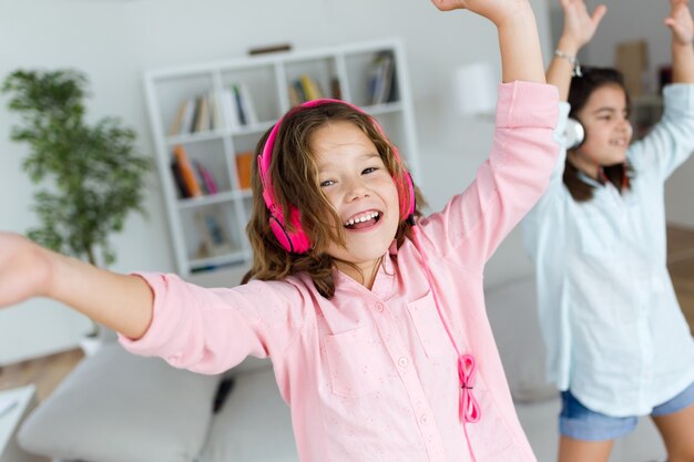 Two young sisters listening to music and dancing at home.