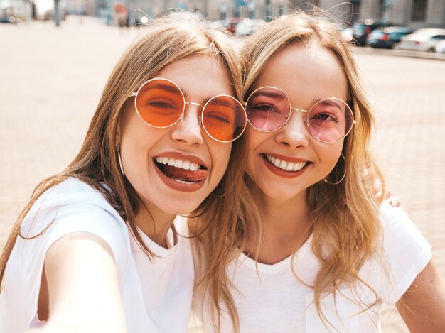 Two young smiling hipster blond women in summer white t-shirt clothes.  