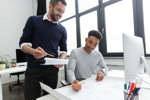 Two young smiling male workers working together with documents