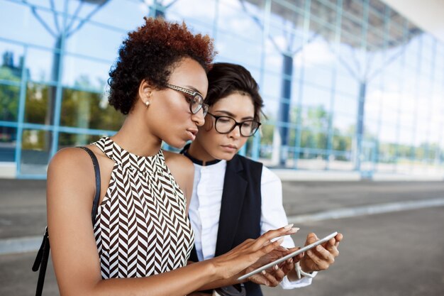 Two young successful businesswomen looking at tablet over business centre.