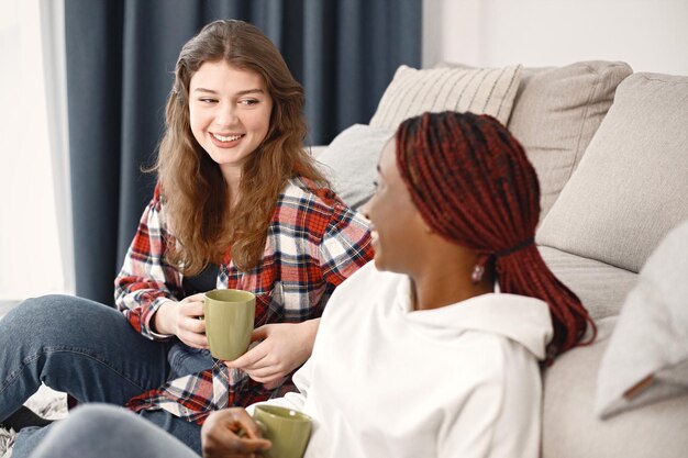 コーチの近くの床に座って話したりお茶を飲んだりする2人の若い10代の少女