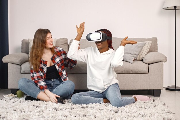 Two young teenage girls sitting on a floor near bed wearing a virtual reality glasses