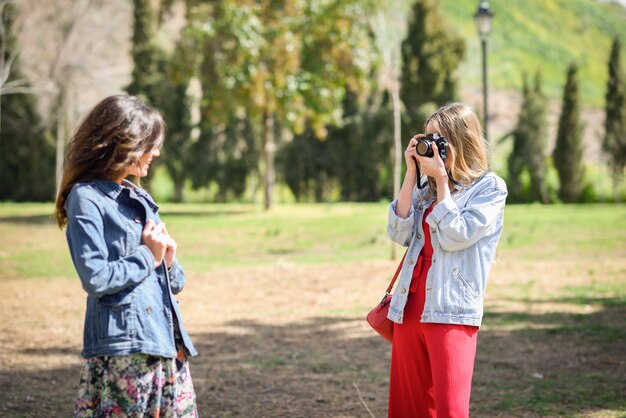 Two young tourist women taking photographs with analogic reflex camera in urban park.