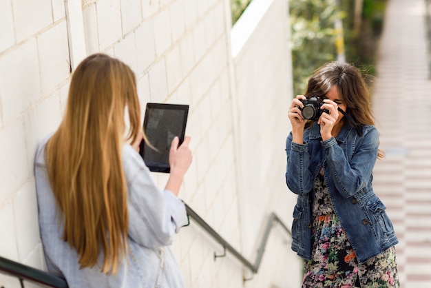 디지털 태블릿 및 아날로그 리플렉스 카메라로 사진을 찍는 두 젊은 관광객 여성