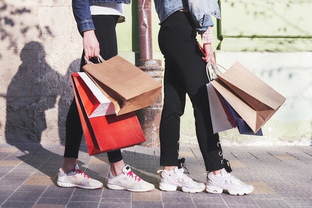 Две молодые женщины, несущие хозяйственные сумки во время прогулки по улице после посещения магазинов.