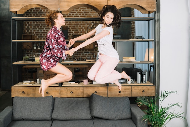 Two young women jumping on sofa at home