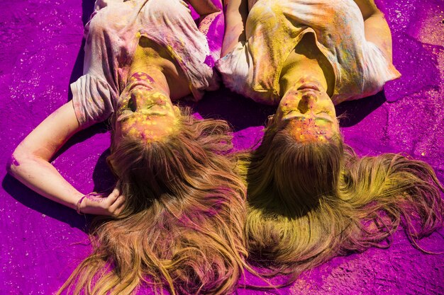 Две молодые женщины лежат на фиолетовом порошке цвета Холи