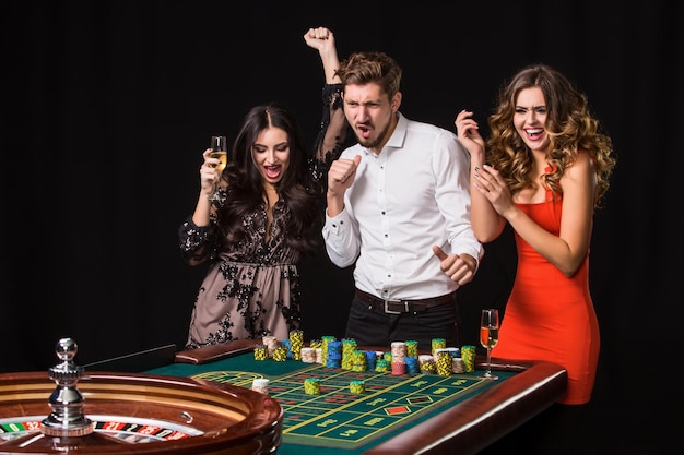 Free photo two young women and man behind roulette table on black background. emotions players