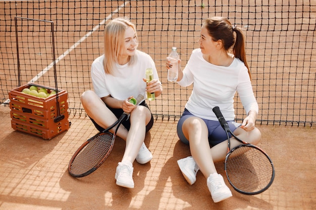 Due giovani donne sedute vicino alla rete da tennis. conversazione dopo partita