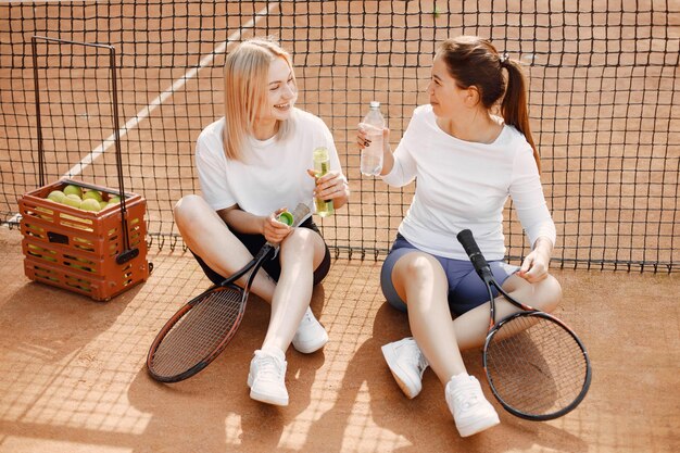 Two young women sitting by tennis net. Having conversation after game