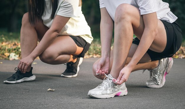 Free photo two young women tying their shoelaces before jogging in the park healthy lifestyle working out together