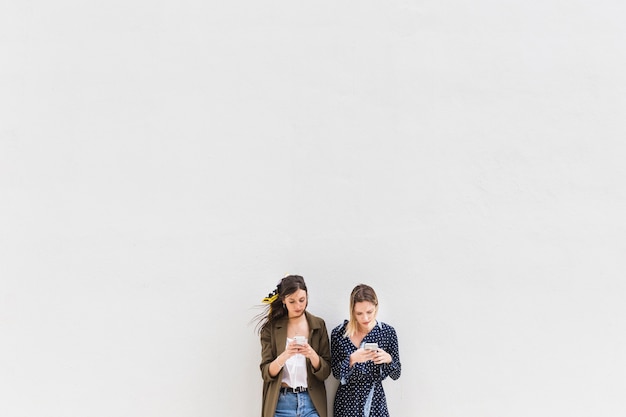 Free photo two young women using cellphones against white background