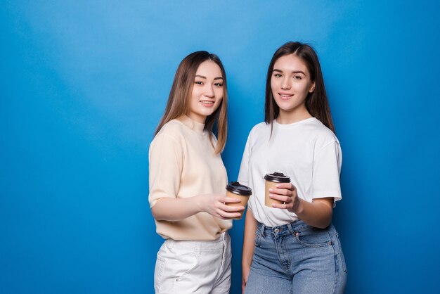 Две молодые женщины с чашкой кофе, чтобы пойти изолированы на синей стене