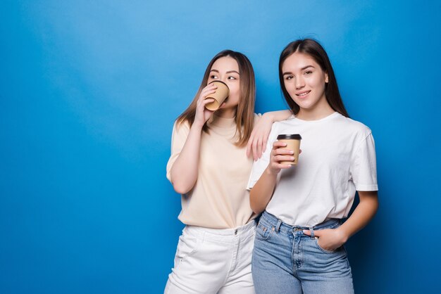 Two young women with coffee cup to go isolated on blue wall